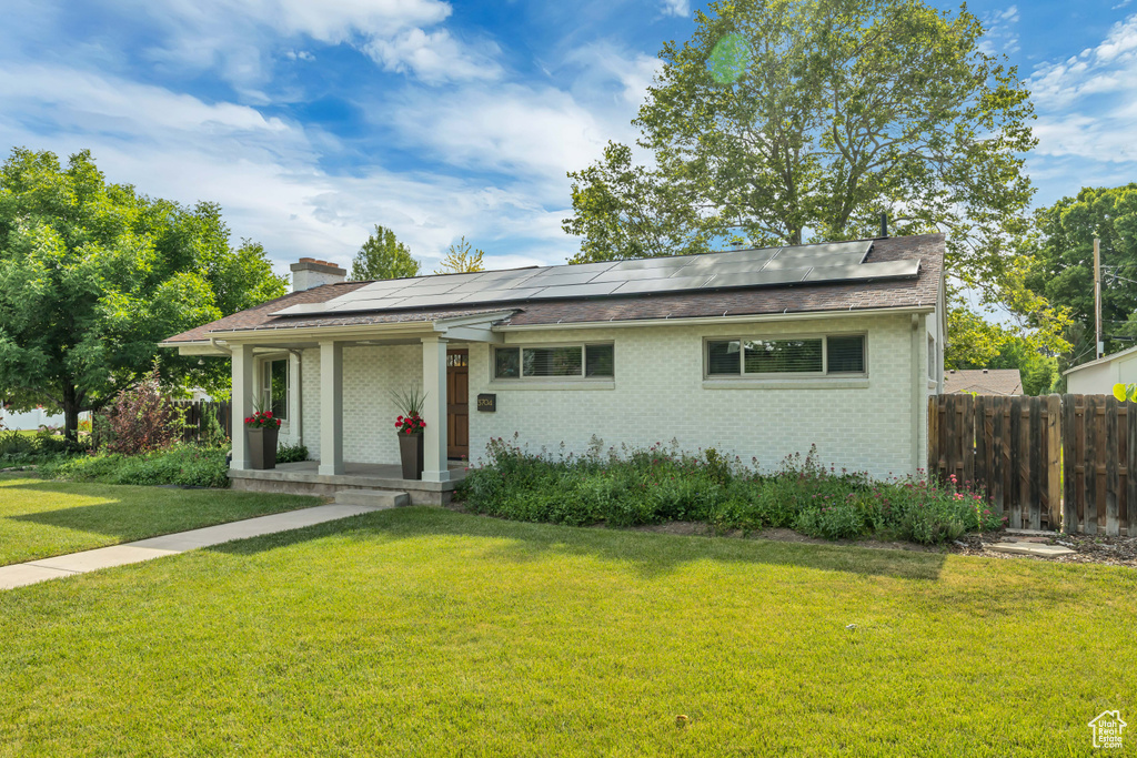View of front facade featuring solar panels, brick siding, a chimney, and a shingled roof