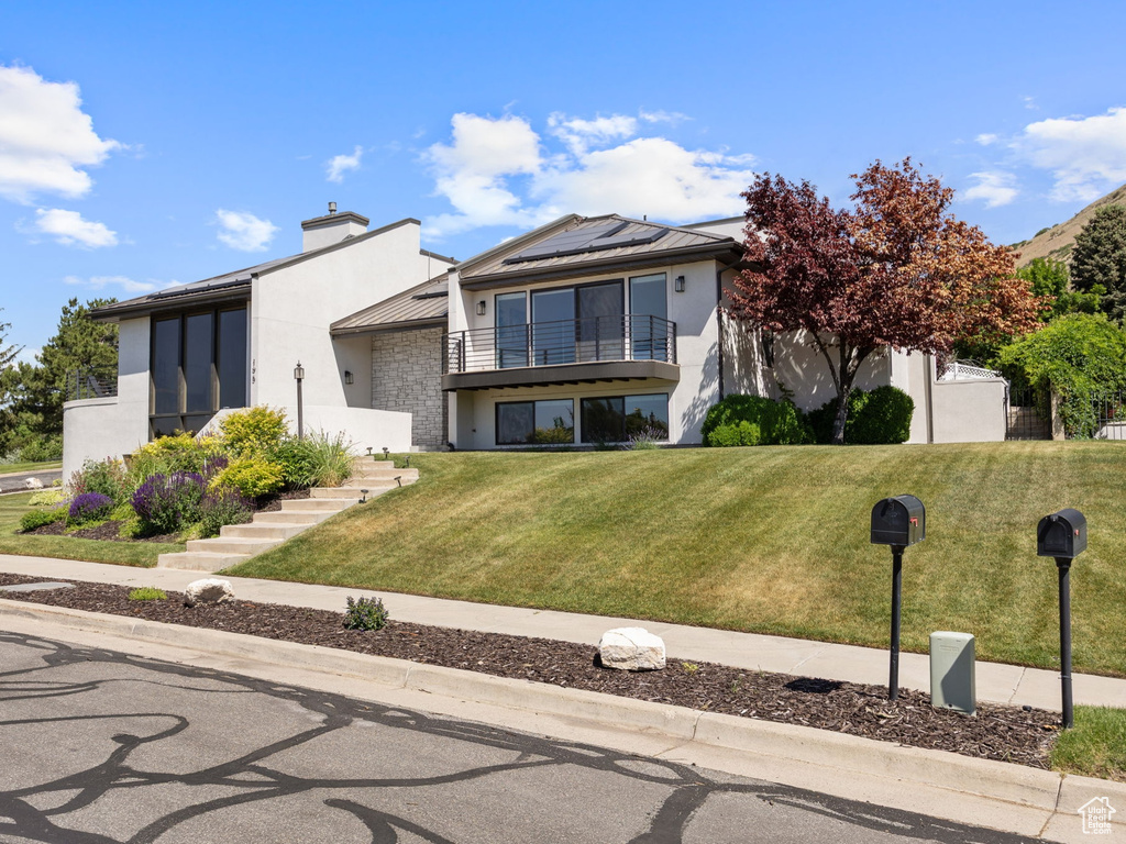 View of front of home with a balcony, a standing seam roof, stucco siding, solar panels, and a metal roof
