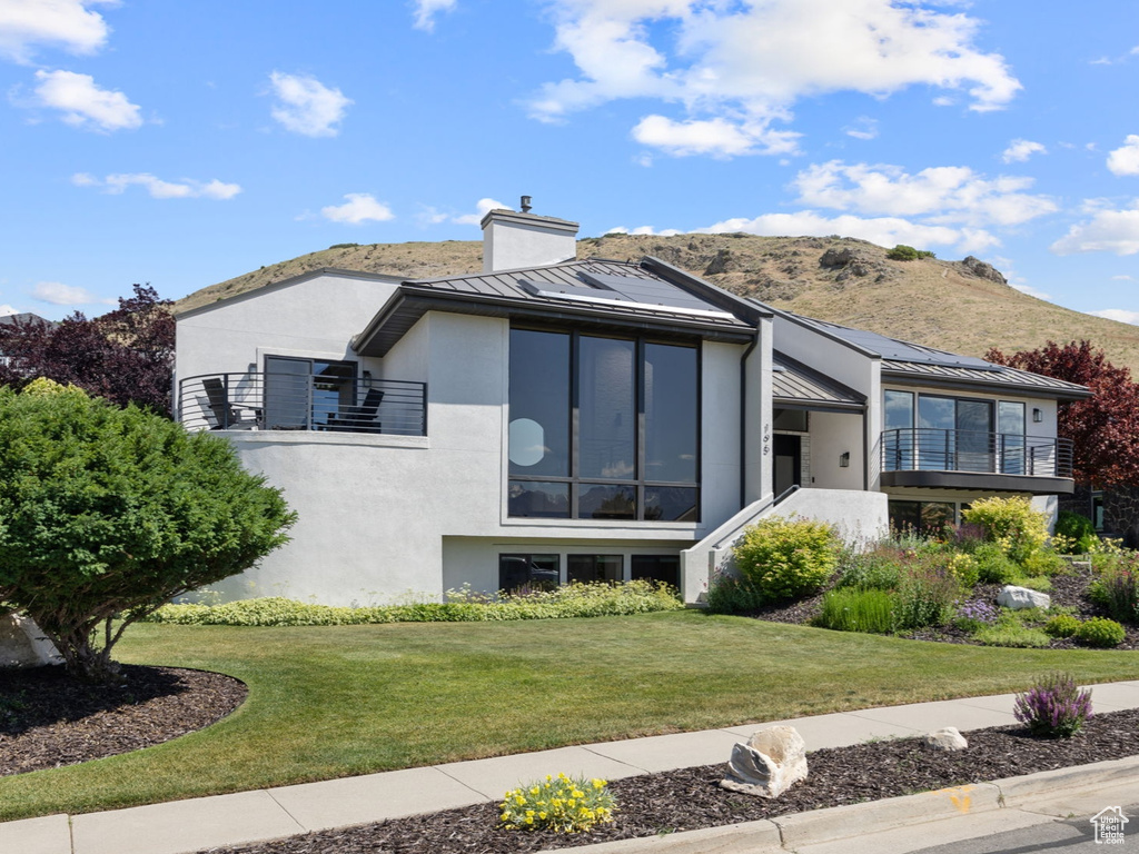 Back of property featuring a balcony, a chimney, stucco siding, a yard, and a mountain view