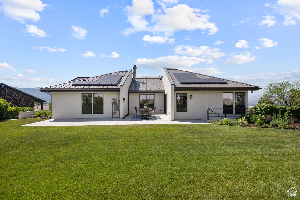 Back of property featuring a standing seam roof, a metal roof, stucco siding, a patio area, and roof mounted solar panels