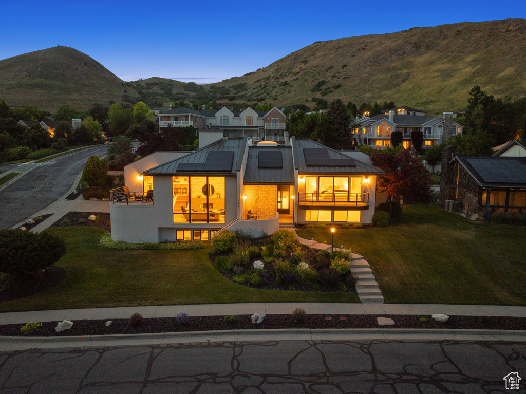 View of front of house featuring a standing seam roof, roof mounted solar panels, a balcony, a front yard, and a mountain view