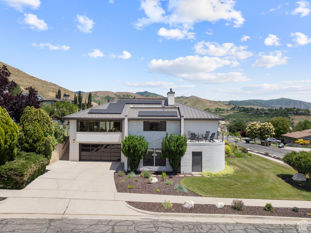 View of front facade with a mountain view, driveway, roof mounted solar panels, and a standing seam roof