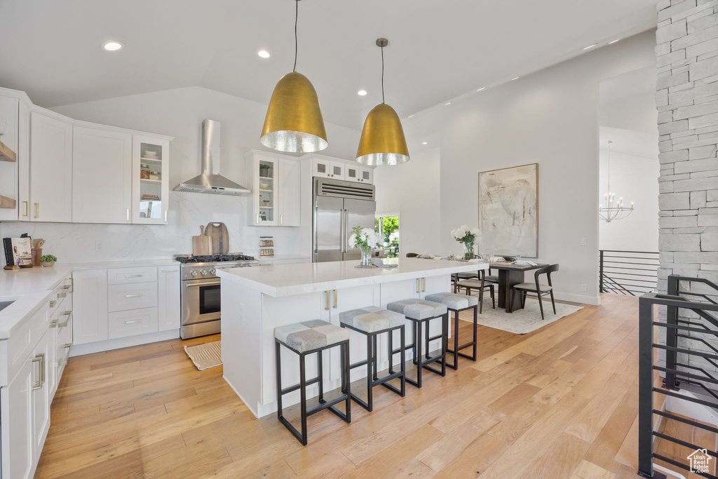 Kitchen with wall chimney exhaust hood, premium appliances, a breakfast bar, white cabinetry, and a center island