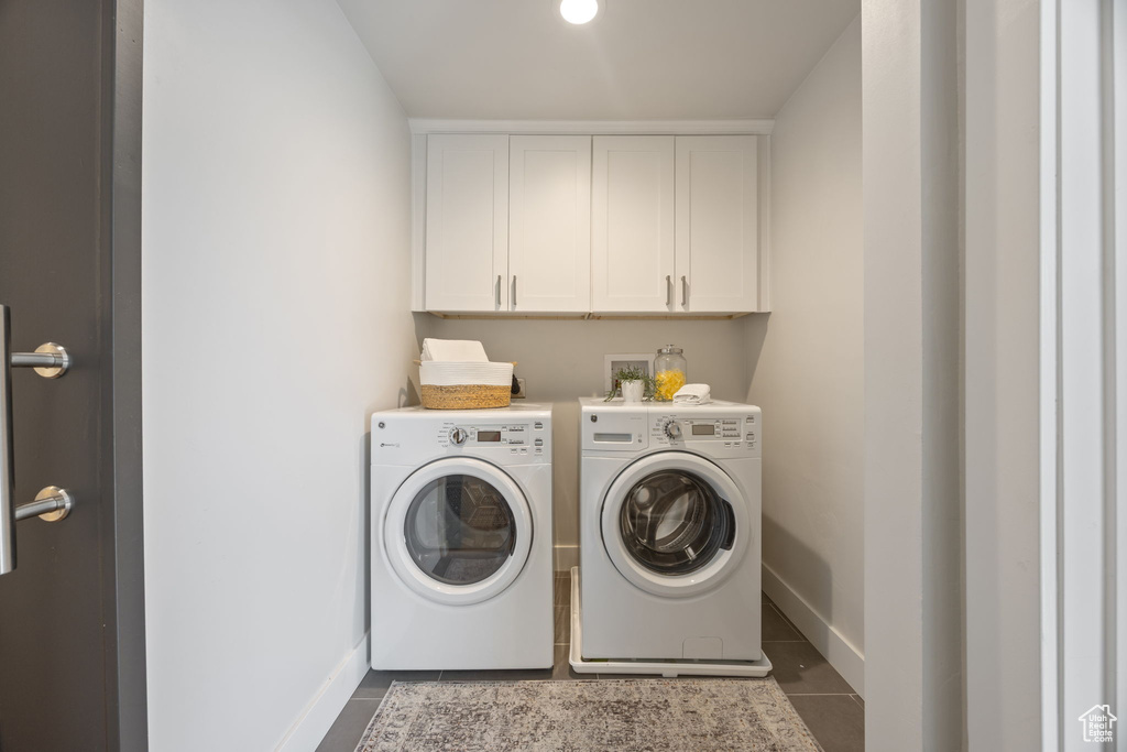 Washroom with washer and clothes dryer, dark tile patterned floors, and cabinet space