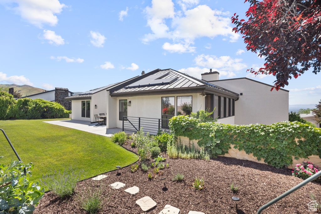 Rear view of house with a standing seam roof, a chimney, a patio area, a metal roof, and stucco siding
