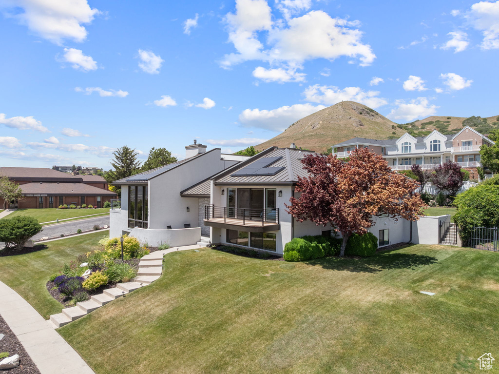 Rear view of property with solar panels, a standing seam roof, stucco siding, a chimney, and a metal roof
