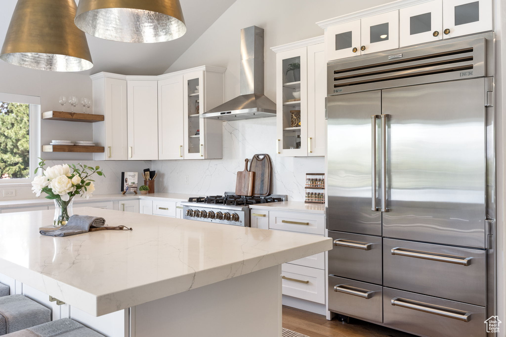 Kitchen featuring built in fridge, wall chimney exhaust hood, open shelves, white cabinets, and vaulted ceiling