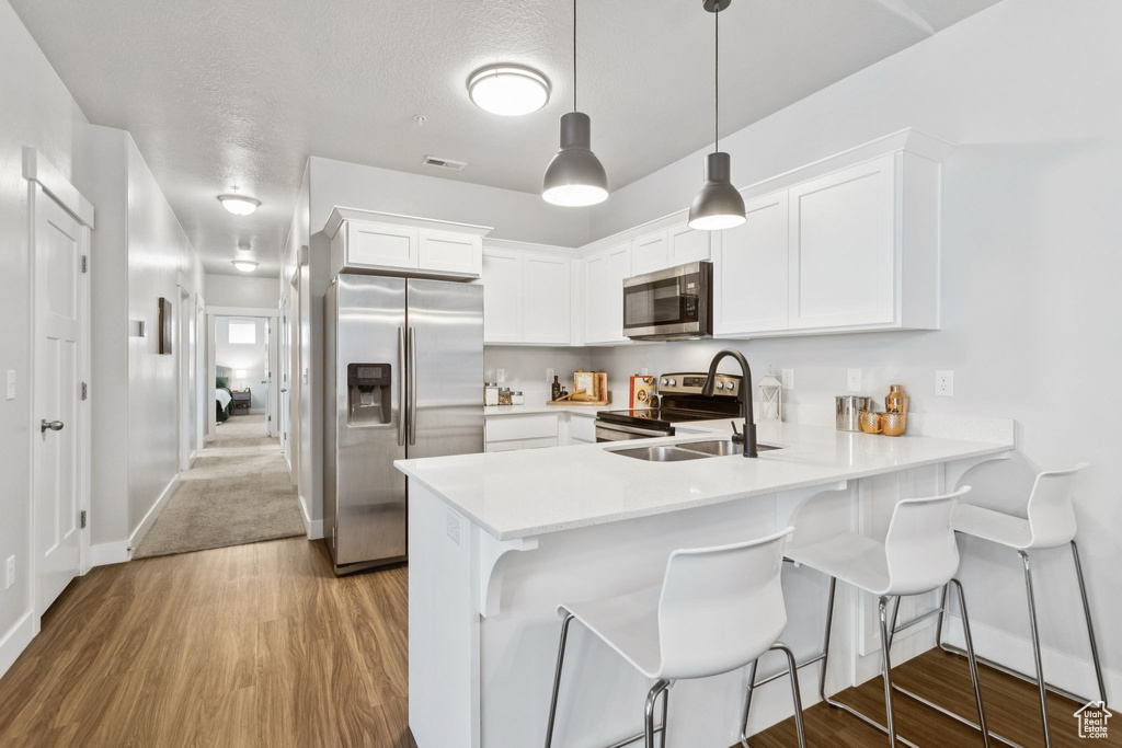 Kitchen with stainless steel appliances, a peninsula, light countertops, white cabinetry, and wood finished floors