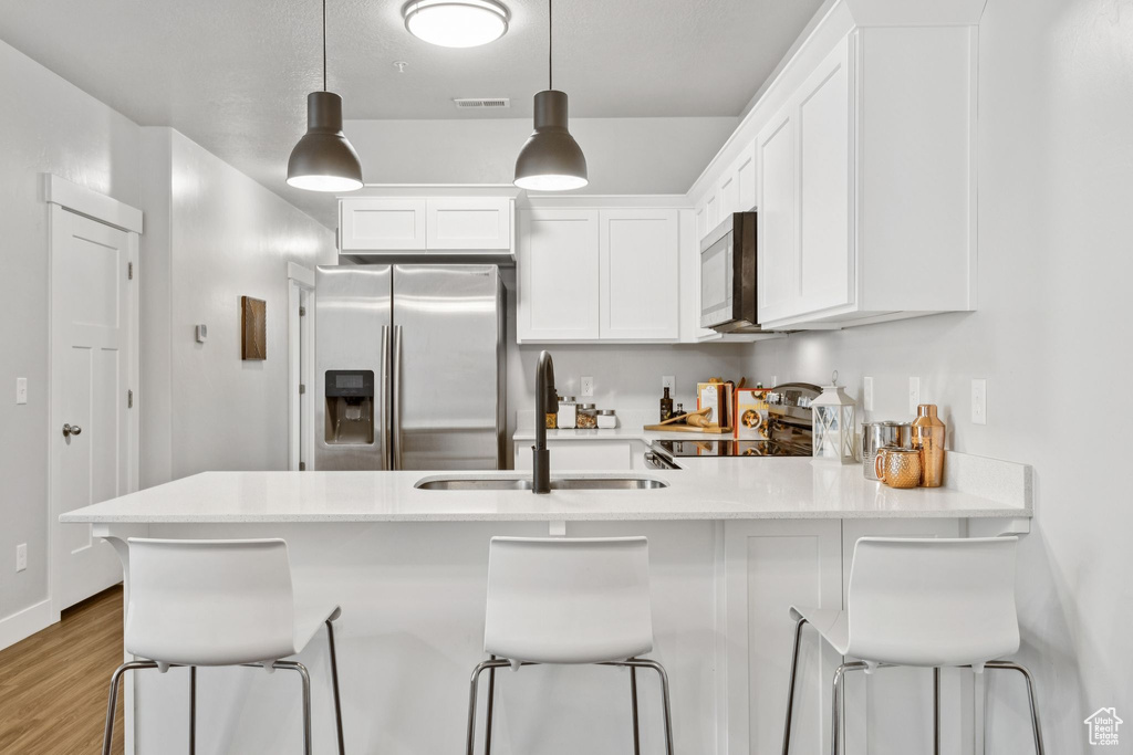 Kitchen featuring stainless steel appliances, white cabinets, a peninsula, light countertops, and wood finished floors