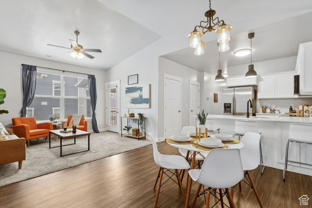 Dining area with vaulted ceiling, wood finished floors, a ceiling fan, and a chandelier