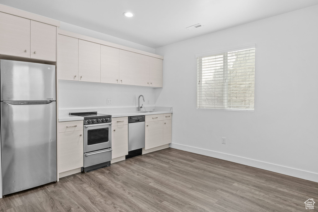 Kitchen with stainless steel appliances, light countertops, light wood-style flooring, recessed lighting, and white cabinets