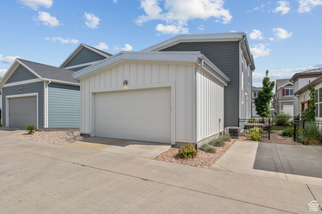 View of front facade with board and batten siding, an attached garage, driveway, and an outbuilding