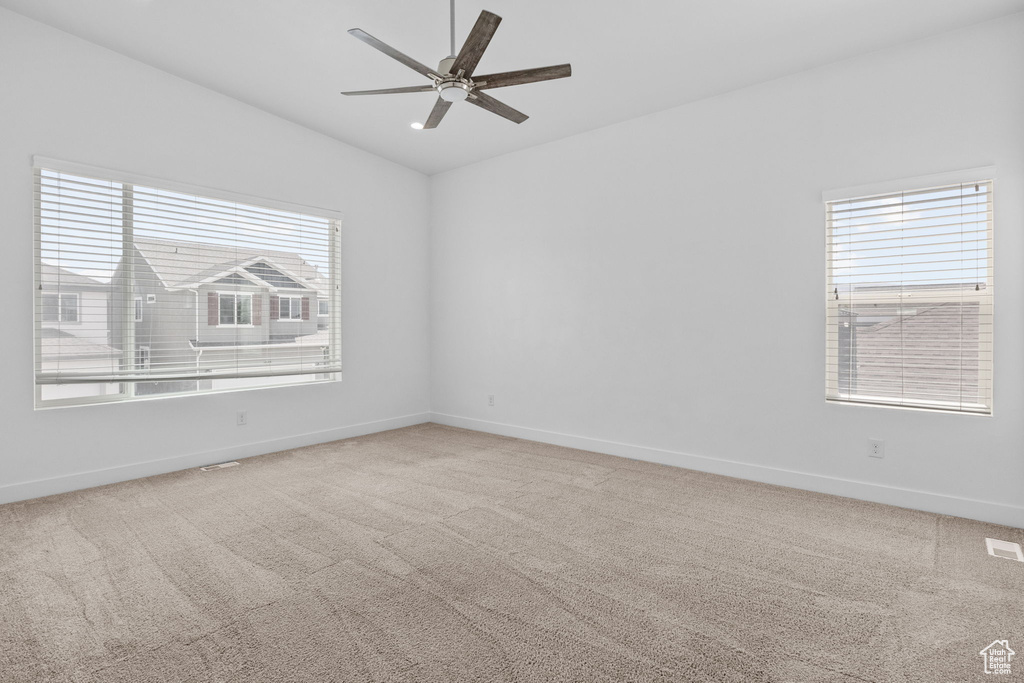 Carpeted empty room with plenty of natural light, vaulted ceiling, and a ceiling fan
