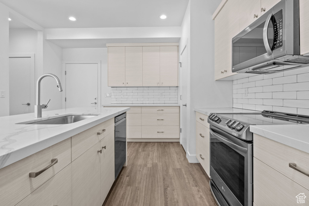 Kitchen with stainless steel appliances, light wood-style flooring, decorative backsplash, recessed lighting, and light stone counters
