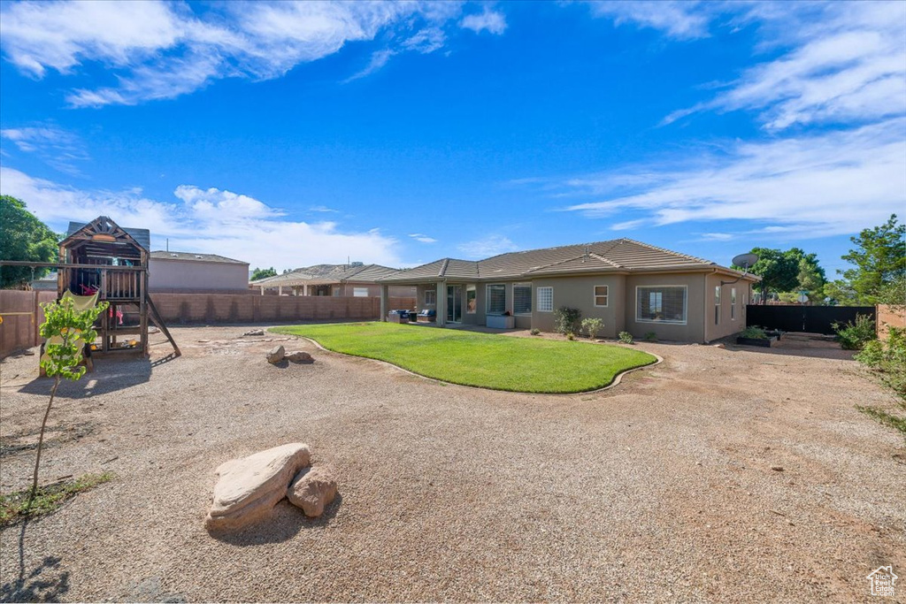 Rear view of house featuring a fenced backyard, a playground, stucco siding, and a tile roof