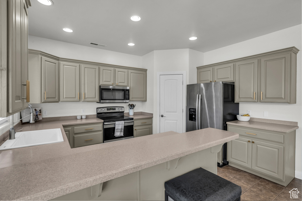 Kitchen with appliances with stainless steel finishes, a peninsula, gray cabinetry, a breakfast bar, and recessed lighting