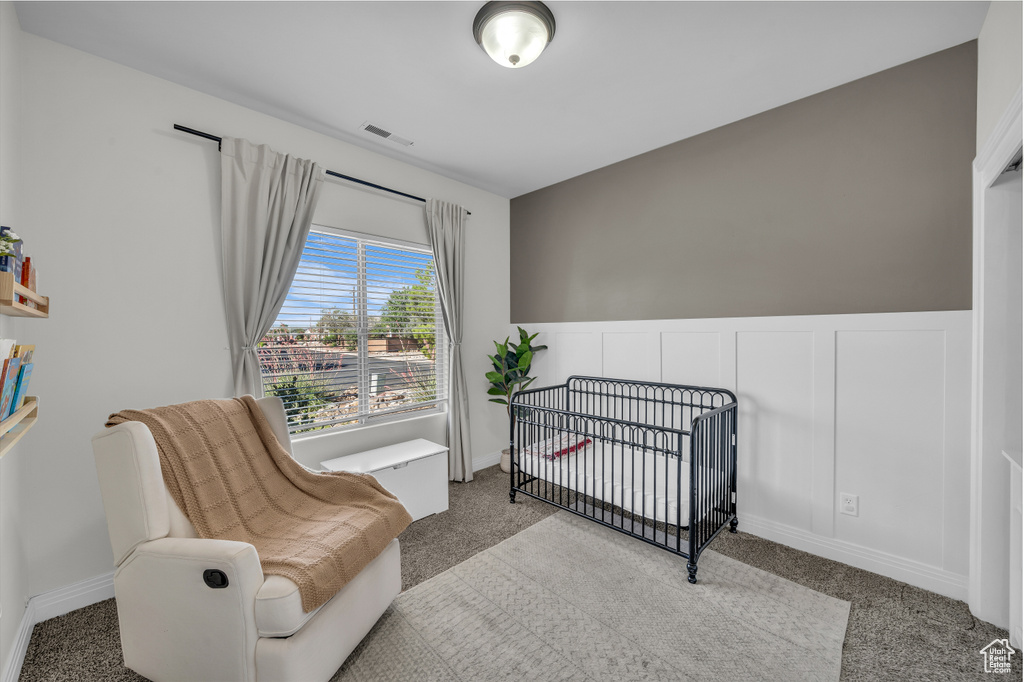 Carpeted bedroom featuring a crib and wainscoting