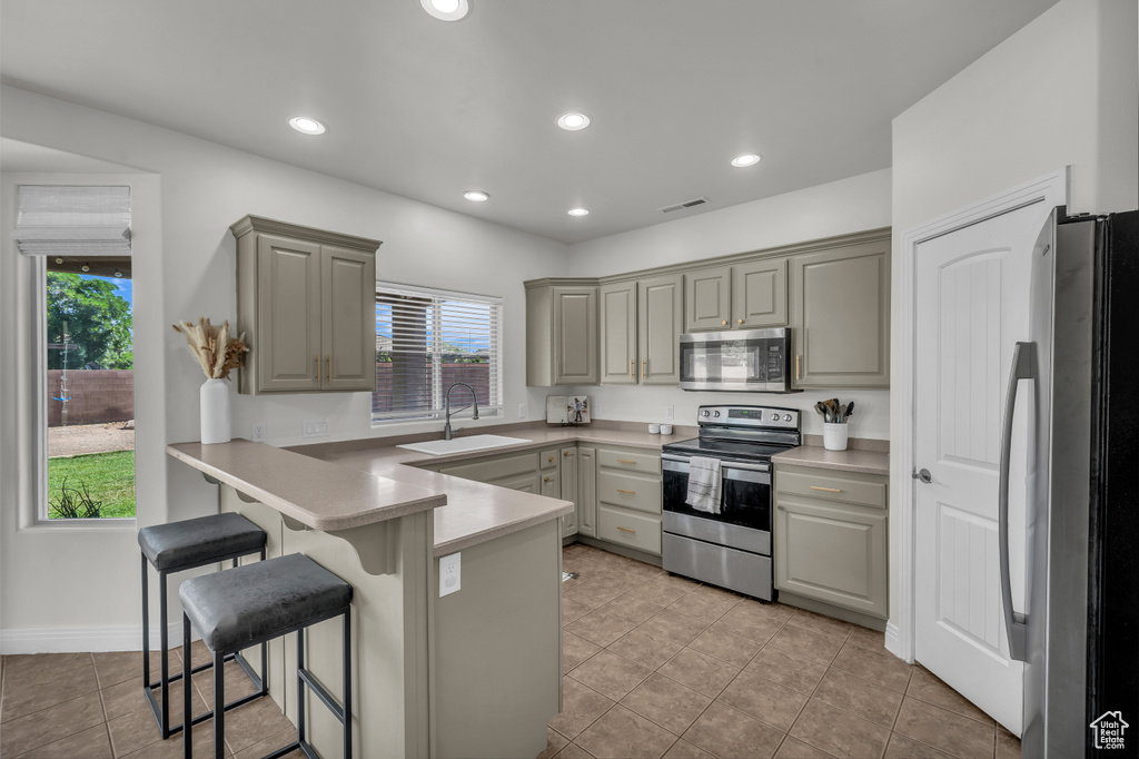 Kitchen with appliances with stainless steel finishes, a peninsula, gray cabinetry, a breakfast bar area, and light tile patterned floors