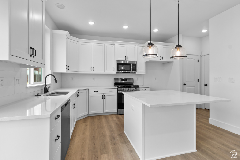 Kitchen with appliances with stainless steel finishes, light wood-type flooring, tasteful backsplash, white cabinets, and recessed lighting
