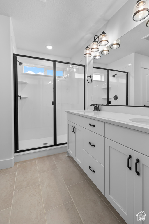 Full bath with double vanity, a stall shower, a textured ceiling, and tile patterned flooring