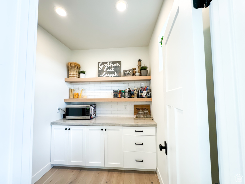 Indoor dry bar featuring stainless steel microwave, tasteful backsplash, light wood finished floors, and recessed lighting
