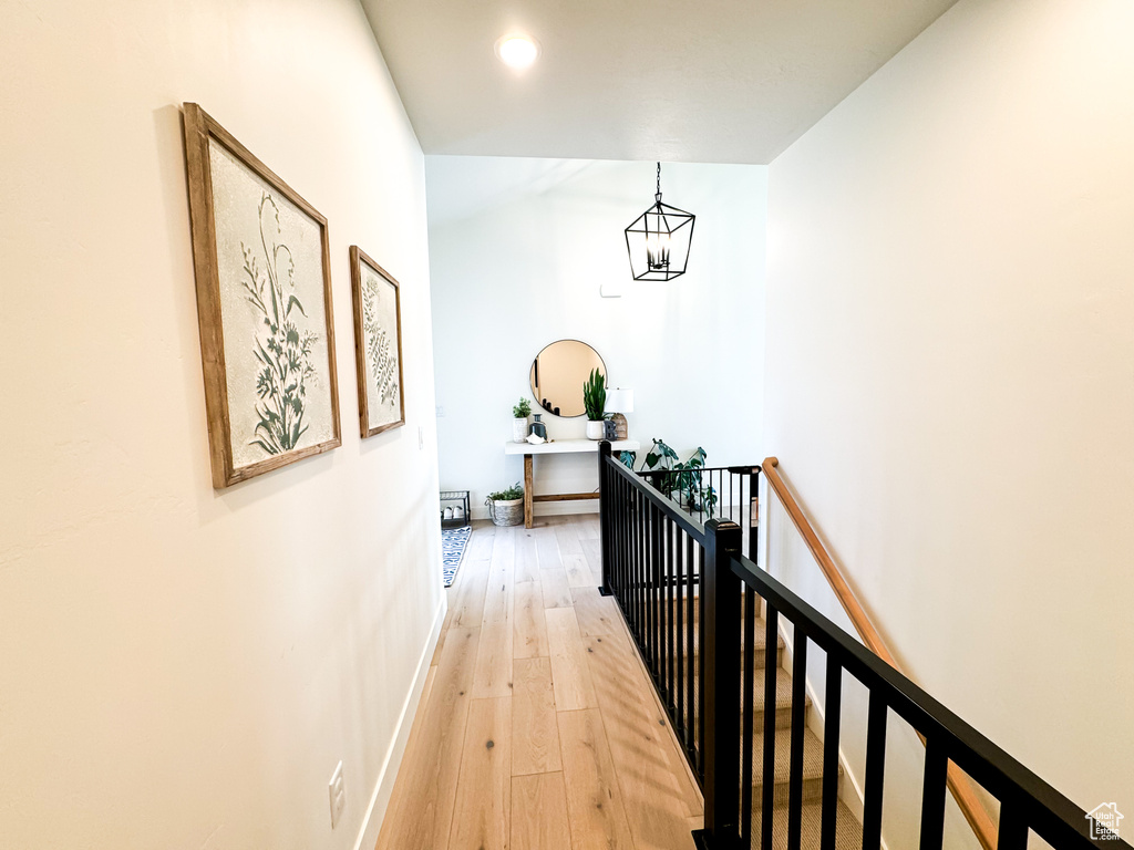 Corridor with an upstairs landing, light wood-style floors, and a chandelier