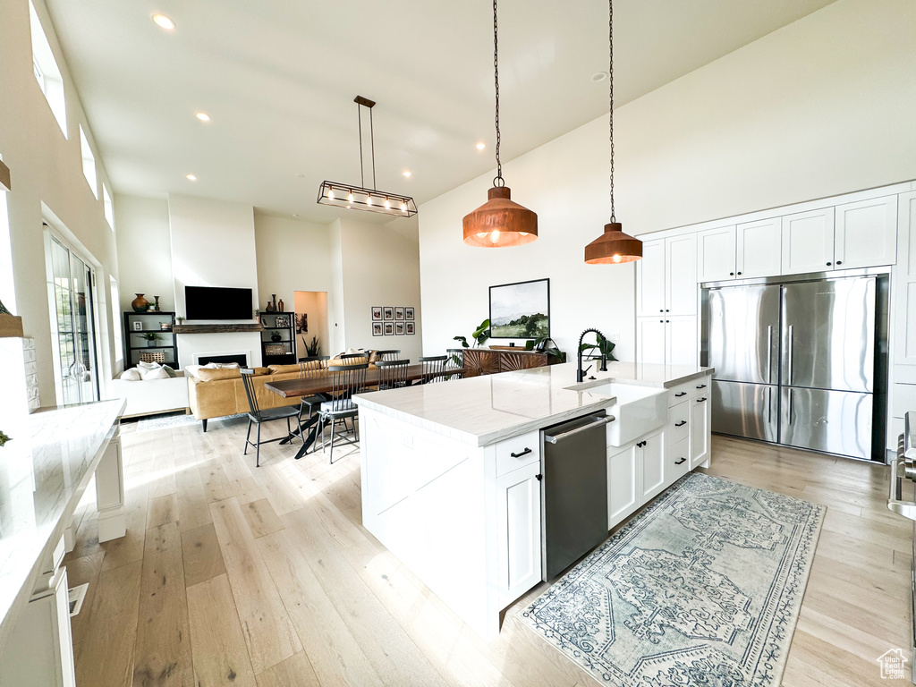 Kitchen with stainless steel appliances, a high ceiling, white cabinetry, light stone counters, and hanging light fixtures