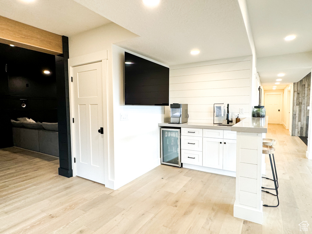 Kitchen with beverage cooler, white cabinetry, light wood-type flooring, light countertops, and a kitchen breakfast bar
