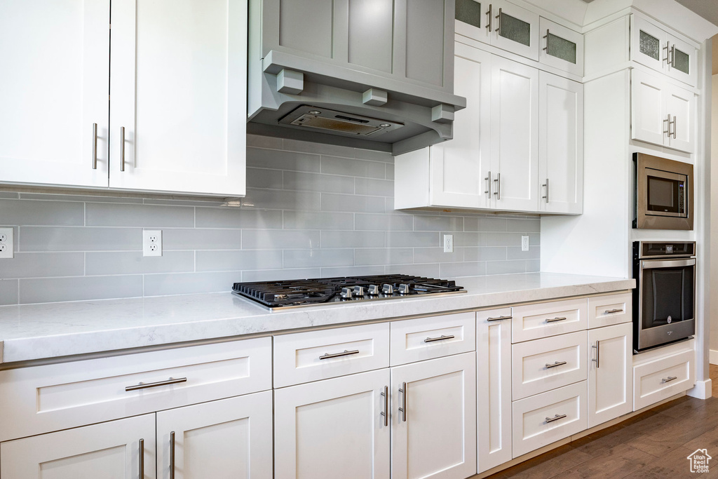 Kitchen with stainless steel appliances, dark wood finished floors, white cabinets, glass insert cabinets, and backsplash