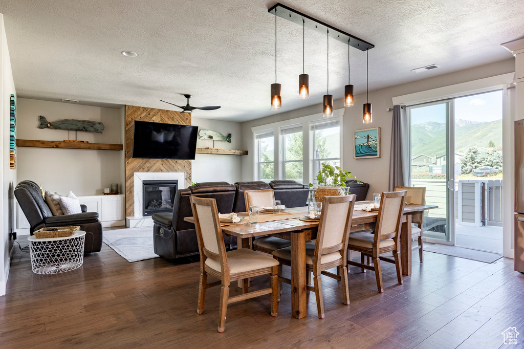 Dining room with a textured ceiling, ceiling fan, plenty of natural light, dark wood-style floors, and a large fireplace