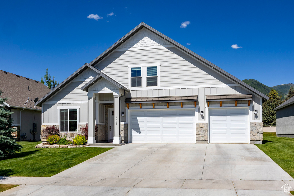 Modern farmhouse style home with stone siding, driveway, board and batten siding, a front lawn, and a mountain view