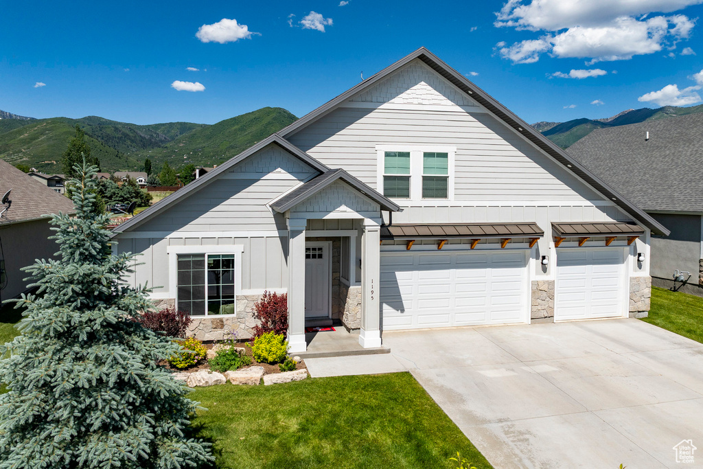 View of front of home with stone siding, a standing seam roof, concrete driveway, and a mountain view