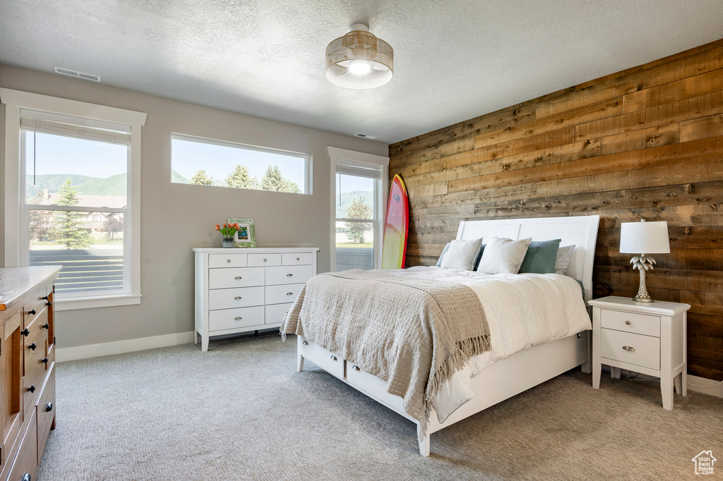 Bedroom with wood walls, multiple windows, light colored carpet, and a textured ceiling