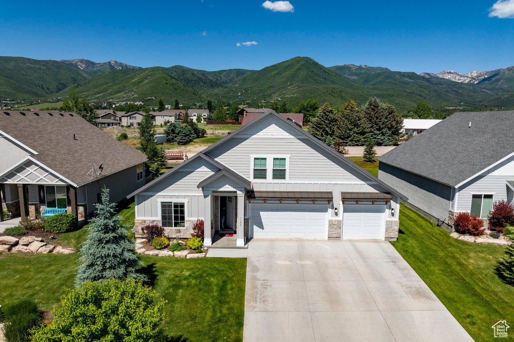View of front of home with board and batten siding, stone siding, concrete driveway, a mountain view, and a front lawn