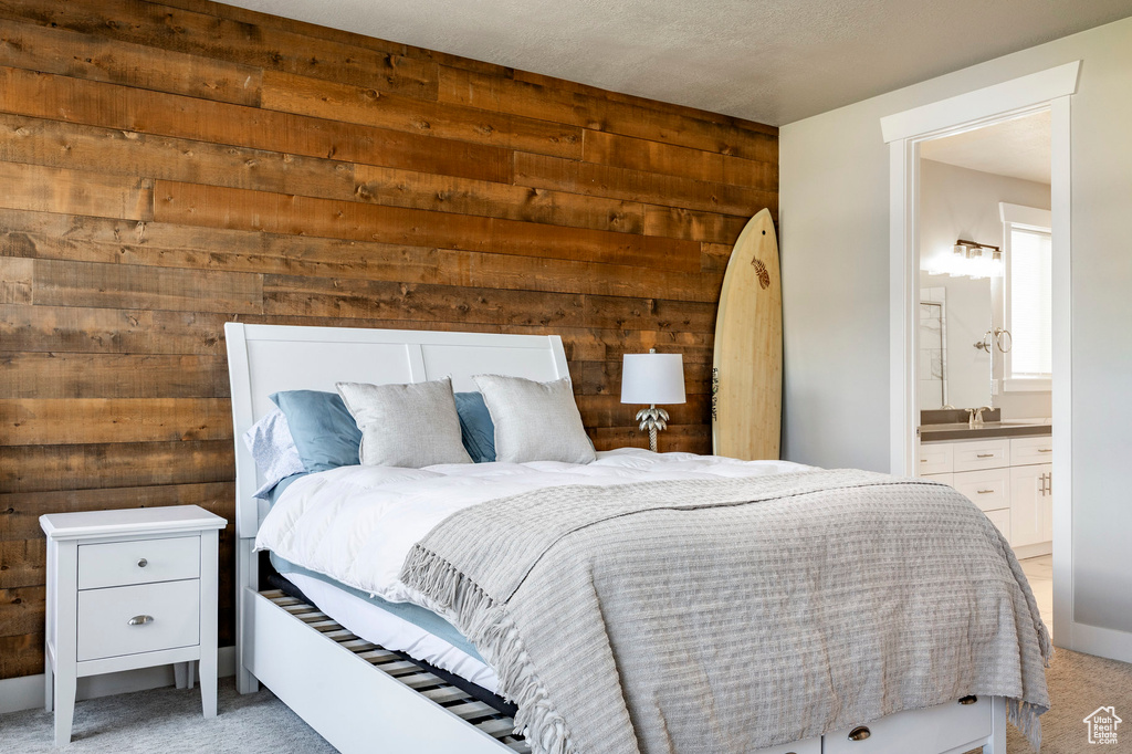 Bedroom with wooden walls, light carpet, and connected bathroom