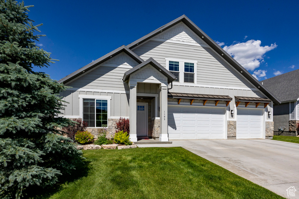 View of front of property with driveway, a front yard, stone siding, and a standing seam roof