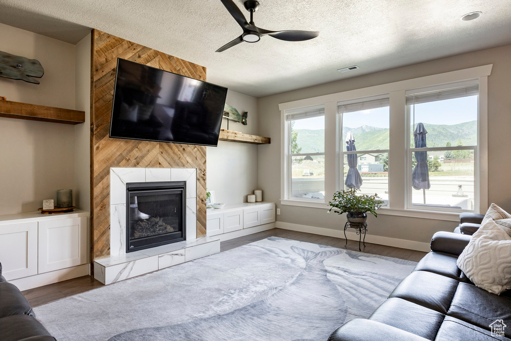 Living area with wood finished floors, a ceiling fan, a tiled fireplace, and a textured ceiling