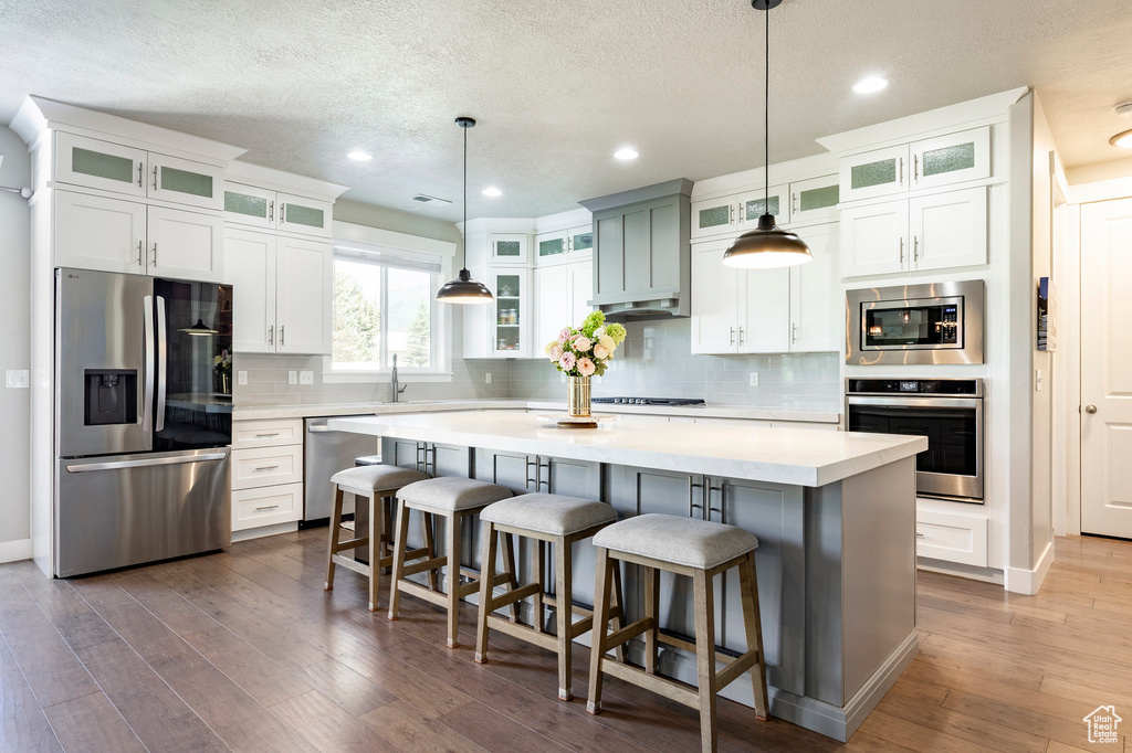 Kitchen featuring appliances with stainless steel finishes, a textured ceiling, backsplash, light countertops, and dark wood-style flooring
