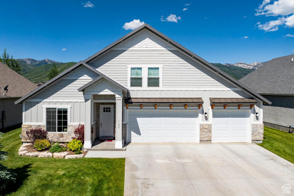 View of front of house with stone siding, concrete driveway, a mountain view, and a standing seam roof