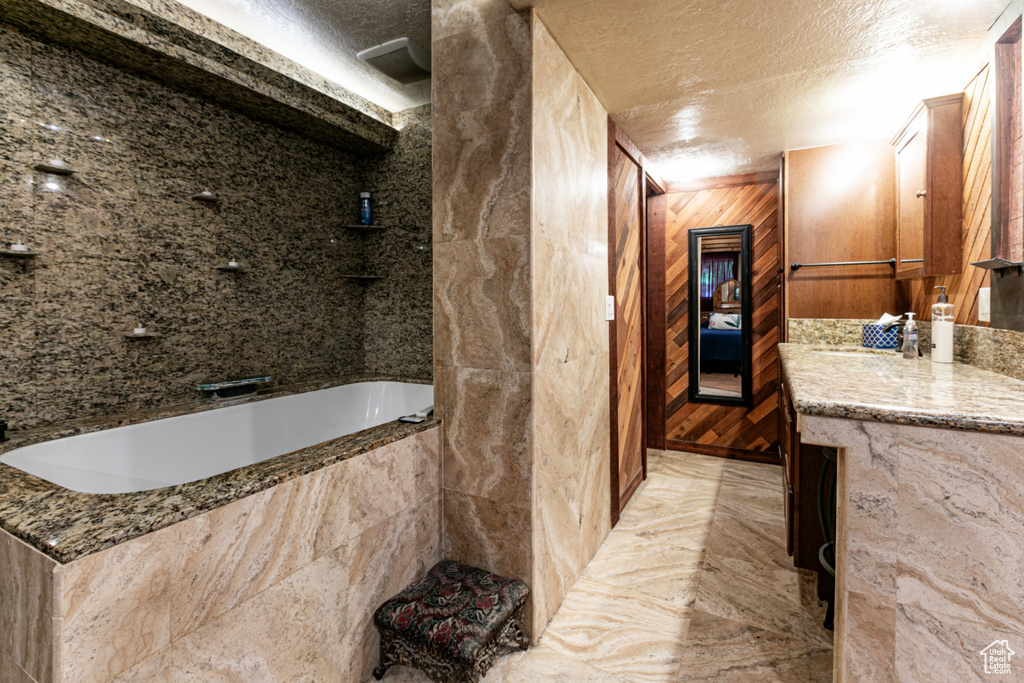 Full bathroom with a relaxing tiled tub, a textured ceiling, marble finish floors, vanity, and wooden walls