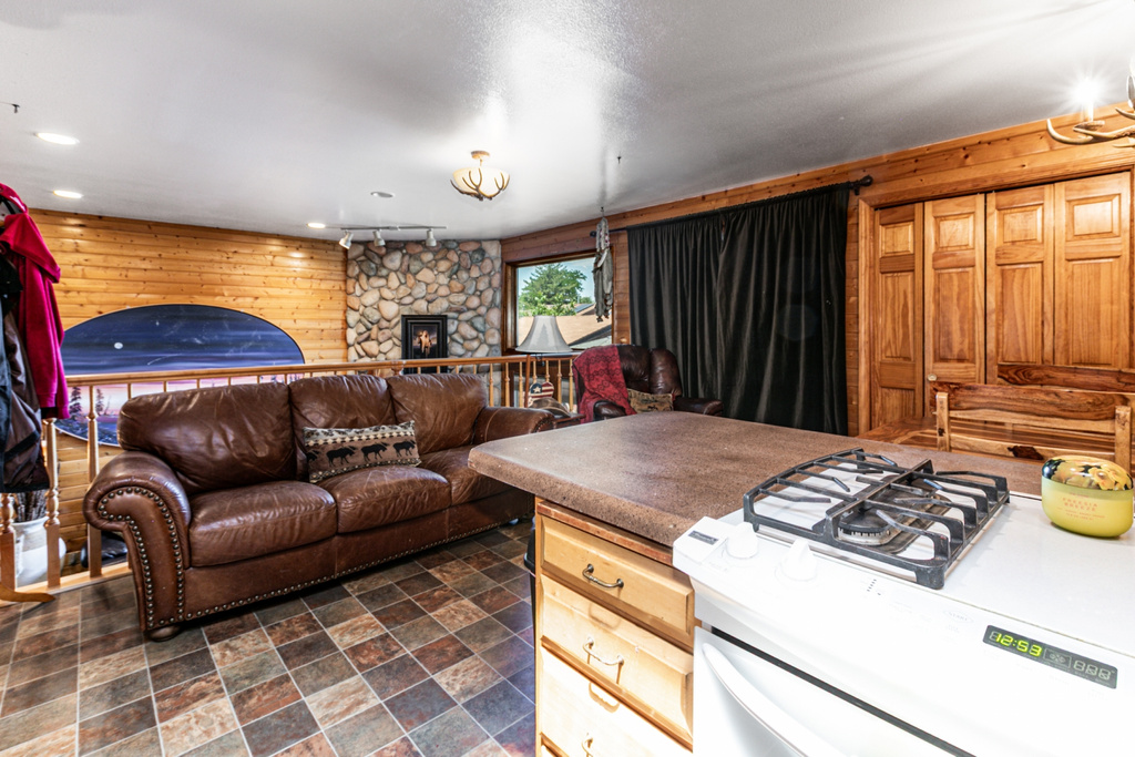 Kitchen featuring wood walls, white range, open floor plan, stone finish flooring, and a stone fireplace
