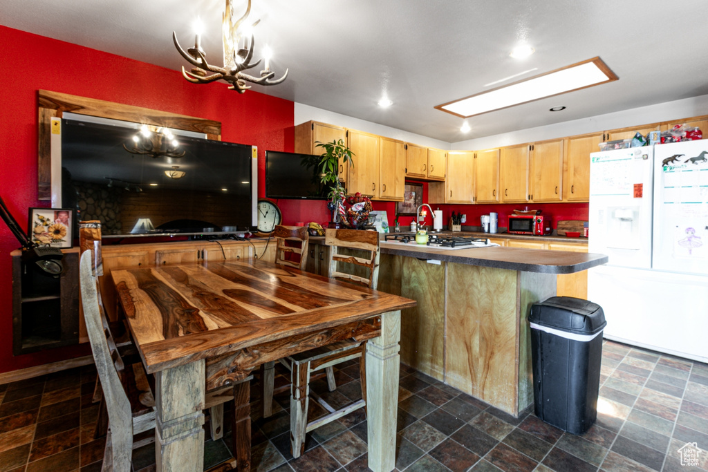 Kitchen featuring white appliances, a chandelier, stone finish flooring, a peninsula, and dark countertops