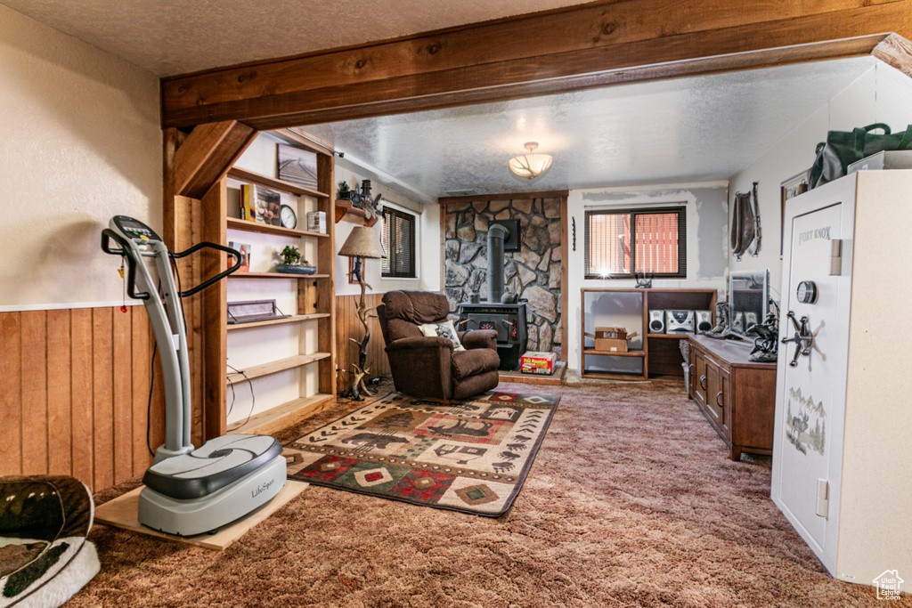 Living area with a wood stove, carpet, a textured ceiling, and wooden walls