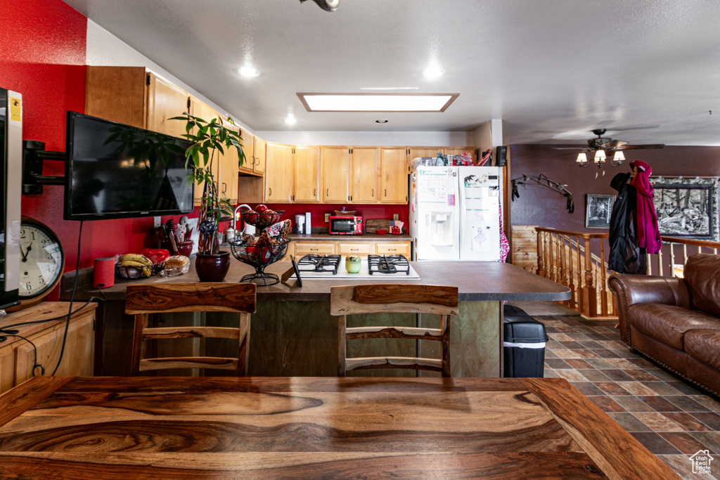 Kitchen featuring white fridge with ice dispenser, dark countertops, a peninsula, gas cooktop, and a ceiling fan