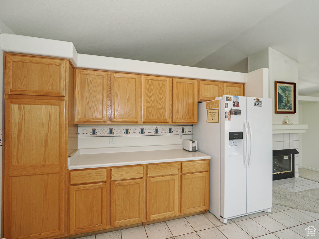 Kitchen with white refrigerator with ice dispenser, light tile patterned floors, light countertops, a tile fireplace, and lofted ceiling