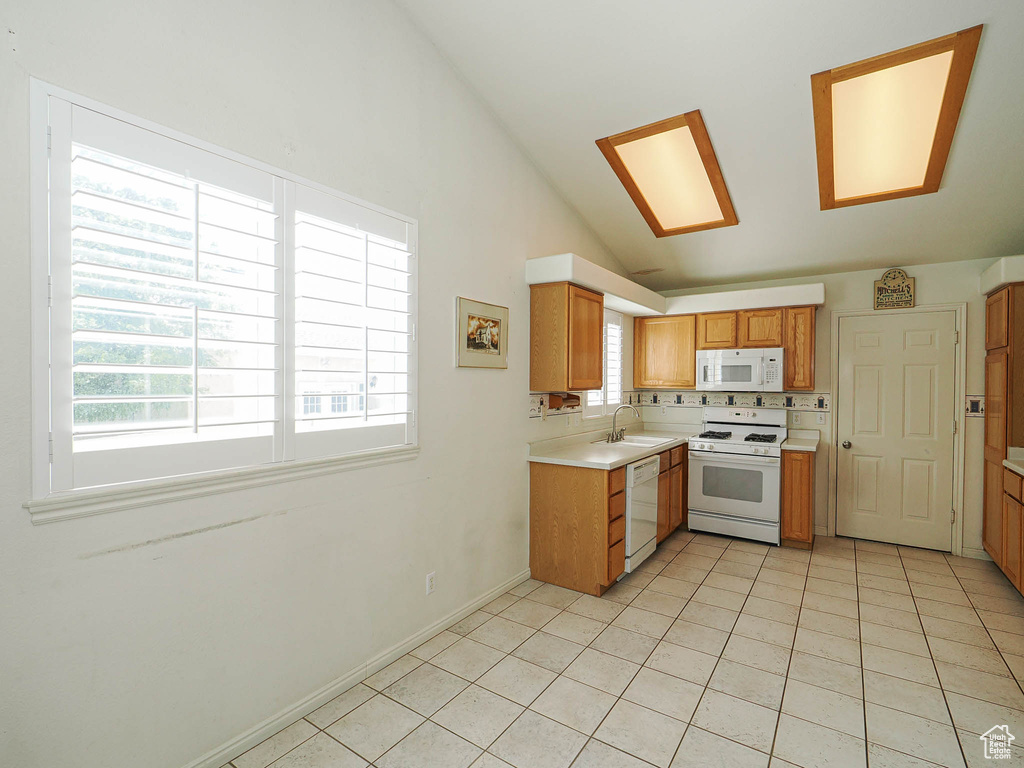 Kitchen featuring white appliances, light countertops, lofted ceiling, light tile patterned flooring, and brown cabinetry