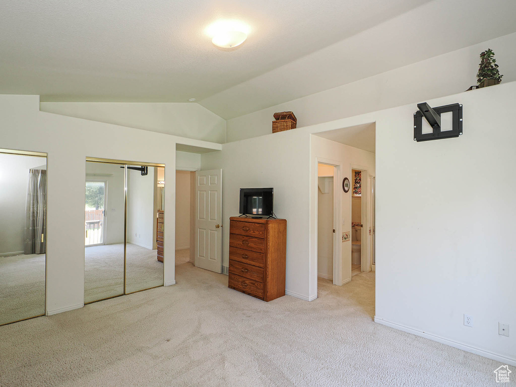 Unfurnished bedroom featuring two closets, light carpet, and lofted ceiling
