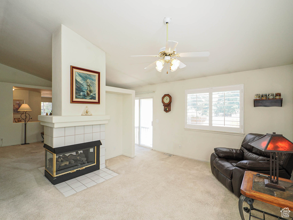 Living area featuring carpet floors, a ceiling fan, a tiled fireplace, and lofted ceiling
