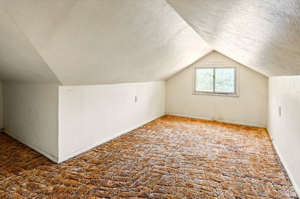 Bonus room featuring a textured ceiling, vaulted ceiling, carpet flooring, and baseboards