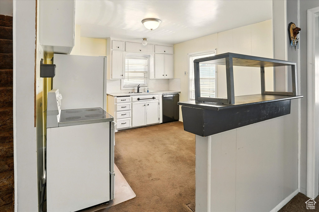 Kitchen featuring dishwashing machine, stove, light colored carpet, and white cabinets